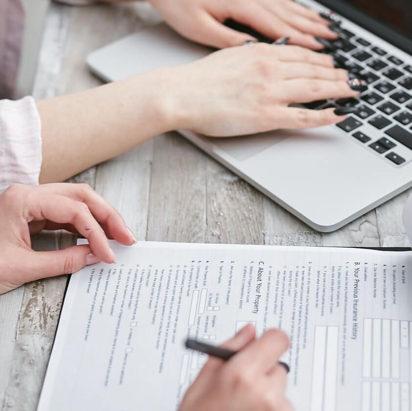 Hands filling in a paper personal loan application form next to a laptop